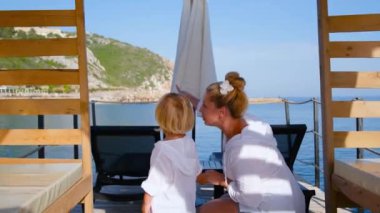 Anne ve oğluna beyaz gömlekli bir şey gösterir.