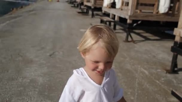 Liten pojke i en vit skjorta vid havet springer mot kameran — Stockvideo