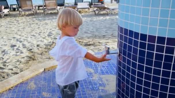 Liten pojke leker med vatten i en kran på stranden — Stockvideo