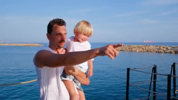 Pai segura seu filho em seus braços e mostra-lhe algo com um dedo em camisas brancas — Vídeo de Stock