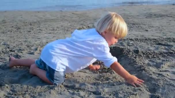 Petit garçon dans une chemise blanche joue dans le sable sur la plage — Video