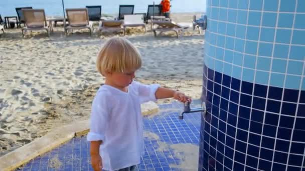 Liten pojke leker med vatten i en kran på stranden — Stockvideo