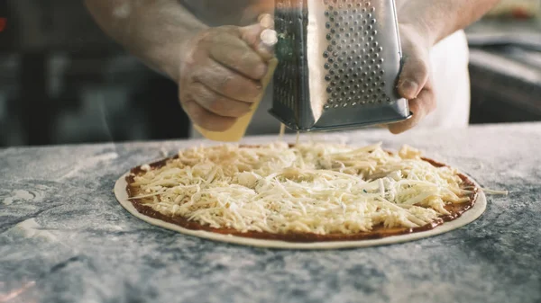 Close up for cooks hands grating cheese on the pizza Four Cheeses.Chef adding the ingredients to the pizza, production and delivery of food. High quality 4k footage