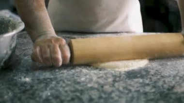 Yakından erkek eli, hamur işini taş bir masanın üzerine ahşap bir raptiyeyle uzatıyor. Camın arkasını görüyor. Yüksek kalite 4k görüntü