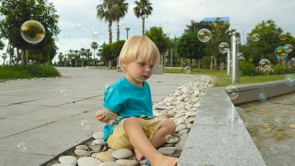 Ένα Μικρό Παιδί Κάθεται Πέτρες Και Βλέπει Σαπουνόφουσκες Υψηλής Ποιότητας — Φωτογραφία Αρχείου