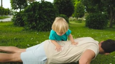 Çocuk babasının sırtına binerken, baba da parkta yerden şınav çekiyor. Yüksek kalite 4k görüntü