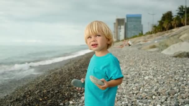 小さな男の子が海岸で遊んでいると 彼は石を水に投げ込む 海による家族の休暇 高品質4K映像 — ストック動画