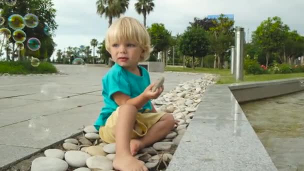 Ένα Μικρό Παιδί Κάθεται Πέτρες Και Βλέπει Σαπουνόφουσκες Υψηλής Ποιότητας — Αρχείο Βίντεο