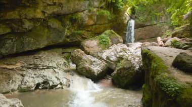 a drone flies over a mountain river through huge rocks to a waterfall. High quality 4k footage