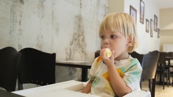 Attractive Boy Eats Banana Sits Table Restaurant Carefully Watching Cartoons — Αρχείο Βίντεο