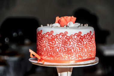 Beautiful wedding cake in white glaze, decorated with red decor on a dark background
