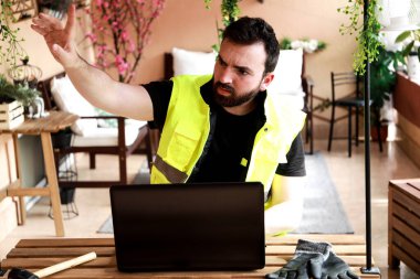 Çalışma alanında bir bilgisayar, eldiven ve çekiçle çalışan bir işçi.