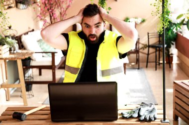 Çalışma alanında bir bilgisayar, eldiven ve çekiçle çalışan bir işçi.