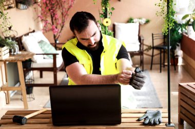 Çalışma alanında bir bilgisayar, eldiven ve çekiçle çalışan bir işçi.