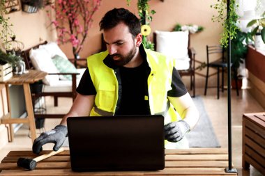 Çalışma alanında bir bilgisayar, eldiven ve çekiçle çalışan bir işçi.