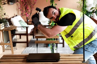 Çalışma alanında bir bilgisayar, eldiven ve çekiçle çalışan bir işçi.