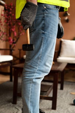 Çalışma alanında bir bilgisayar, eldiven ve çekiçle çalışan bir işçi.