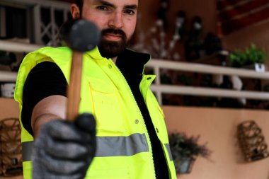 Çalışma alanında bir bilgisayar, eldiven ve çekiçle çalışan bir işçi.