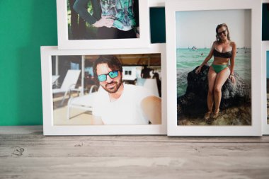 Yazın Mallorca sahillerinde birbirini seven bir çiftin birkaç fotoğrafının beyaz çerçevesi. Gri ahşap arka planı ve mavi-yeşil kumaşı var..