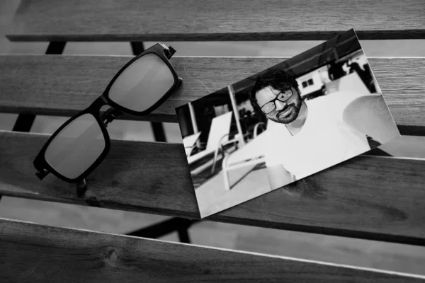 A photo of a handsome, dark-haired boy, wearing sunglasses with blue lenses, on a wooden chair.