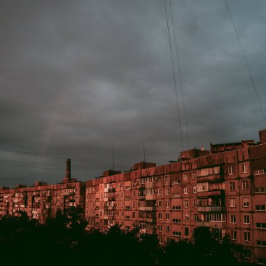 Bulutlar ve evlerin üzerinde zar zor fark edilen bir gökkuşağı.
