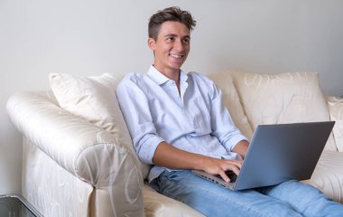 Evdeki kanepede dizüstü bilgisayarla çalışmak zekiceydi. Teknolojisi olan gençler. Uzaktan kumandalı fotoğraf ile modern yaşam tarzı.