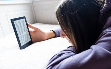 Genç GIrl, Ebook Reader 'ı ile yatakta elektronik romantizm okumaya odaklanmış durumda. Kitap okuyucusundaki metin 