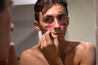 Supporter fan player preparing for fight match with painted face. Coloured face with red
