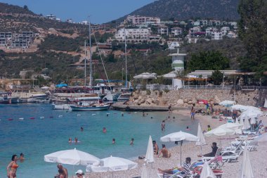 Kalkan, Antalya, Turkey  July 6, 2022: Domestic and foreign vacationers sunbathe on the beach and swim in the sea, the public beach of Kalkan resort 