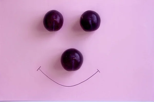 Damson plum on isolated pink background, smile face with red plums
