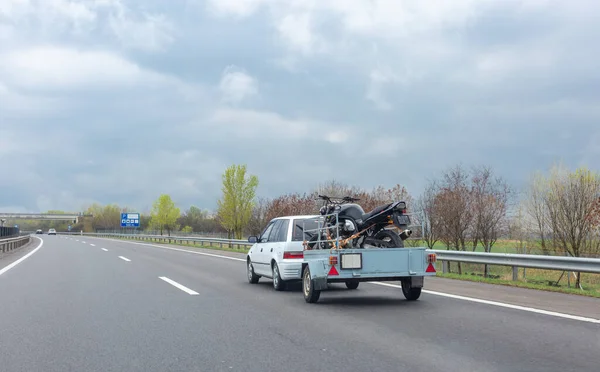 带拖车摩托车的白色汽车在高速公路上行驶 图库图片