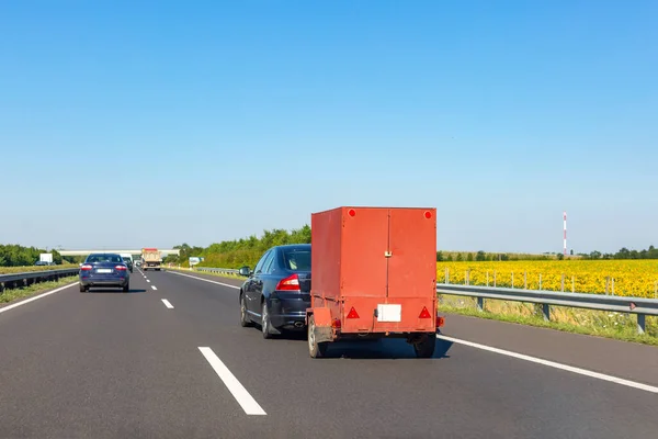 公路上有红色载货拖车的黑色轿车 免版税图库图片