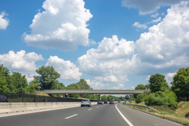 Arabalar yolda. Köprü otoyolda. Yeşil ağaçlarla ve mavi gökyüzünde beyaz bulutlarla güzel bir yaz manzarası.