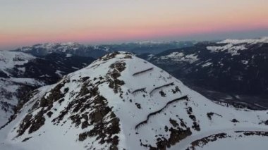 Snowy mountain ski-lifts and furniculars and ski-slopes in Austrian Alps drone flyover the mountains during sunrise golden hour orange sky