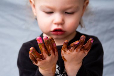 Küçük çocuk parmak boyalarıyla oynadıktan sonra ellerine bakıyor. 