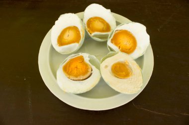 Beyaz tabakta servis edilen tuzlu ördek yumurtası (telur asin) ahşap arka planda izole edilmiş.