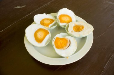 Beyaz tabakta servis edilen tuzlu ördek yumurtası (telur asin) ahşap arka planda izole edilmiş.