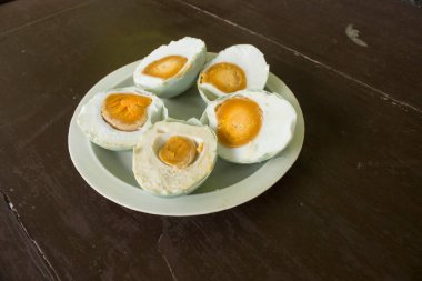 Beyaz tabakta servis edilen tuzlu ördek yumurtası (telur asin) ahşap arka planda izole edilmiş.