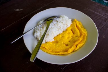 Kızarmış yumurtalı (omlet) bir fotoğraf pilavı, beyaz tabakta çatal ve kaşıkla. Tahta arka planda izole. Sabah omletle kahvaltı