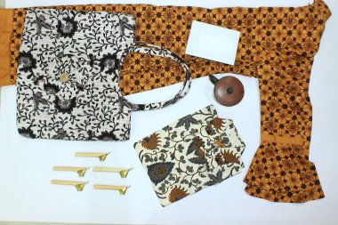 flat lay batik clotes with canting, small pan and wax earthenware glass isolated on white background