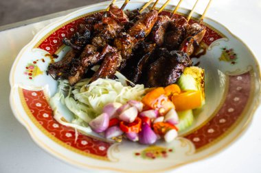 Sate kambing ya da sate klatak ya da kuzu satay ya da keçi eti satay dilimlenmiş lahana, kırmızı soğan, kırmızı biber, soya soslu domates ile servis edilir. izole edilmiş beyaz arkaplan 