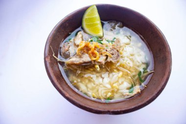 soto kwali. Beyaz arka planda izole edilmiş. Et lahanası, limon ve pirinçli Cava eti çorbası; geleneksel bir kwali kasesinde servis edilir (kilden yapılmış bir kap).)