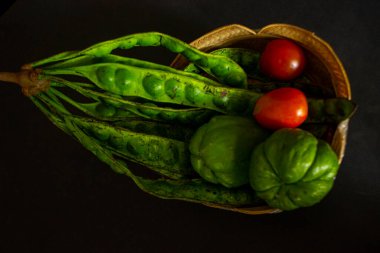 Siyah arka planda izole edilmiş bir sepette tropikal domates, labu siam veya chayote ve soğan servis edilir.
