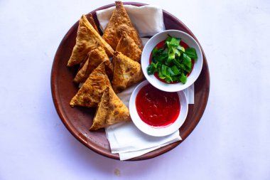 Samosa, samsa veya somsa, siyah arka planda domates sosu ve pırasa dilimi ile servis edilen üç köşeli kızarmış hamur işidir.