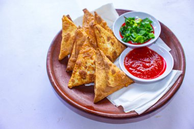 Samosa, samsa veya somsa, siyah arka planda domates sosu ve pırasa dilimi ile servis edilen üç köşeli kızarmış hamur işidir.