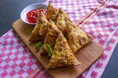 Samosa, samsa veya somsa, siyah arka planda domates sosu ve pırasa dilimi ile servis edilen üç köşeli kızarmış hamur işidir.
