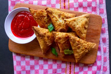 Samosa, samsa veya somsa, siyah arka planda domates sosu ve pırasa dilimi ile servis edilen üç köşeli kızarmış hamur işidir.