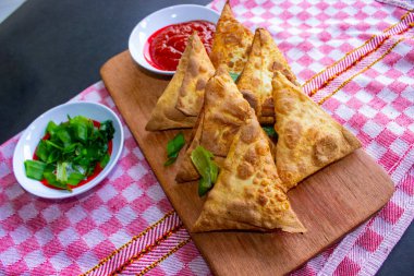 Samosa, samsa veya somsa, siyah arka planda domates sosu ve pırasa dilimi ile servis edilen üç köşeli kızarmış hamur işidir.