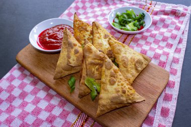 Samosa, samsa veya somsa, siyah arka planda domates sosu ve pırasa dilimi ile servis edilen üç köşeli kızarmış hamur işidir.