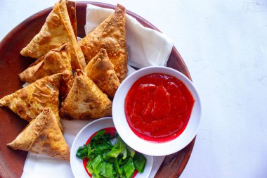 Samosa, samsa veya somsa, siyah arka planda domates sosu ve pırasa dilimi ile servis edilen üç köşeli kızarmış hamur işidir.
